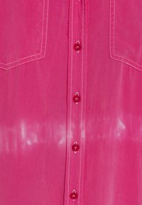 Pink button-up shirt with a smooth texture, featuring front pockets, contrasting white stitching, and glossy pink buttons.