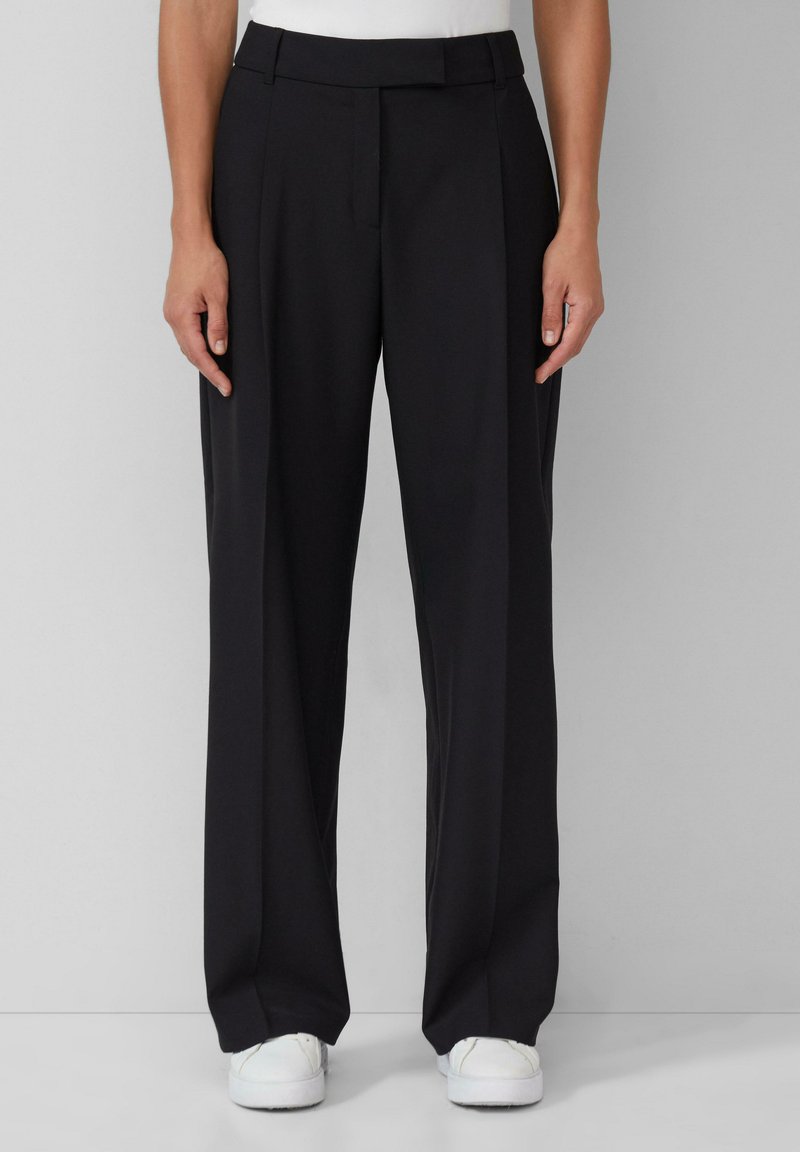 Pantalons noirs ajustés avec une coupe droite, présentant une texture lisse, des plis à l'avant et une taille épurée.