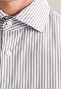 Primo piano di un colletto di una camicia a righe verticali grigie e bianche e dei bottoni nella parte superiore del petto.