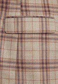 Beżowa tkanina w kratkę w odcieniach brązu i granatu. Zawiera jedną kieszeń z wypustką. Teksturowany splot nadaje głębi wizualnej.