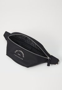 Svart nylon midjeväska med en silverdragkedja, logodetaljer, slät textur och ett mönstrat innerfoder. Kompakt och funktionell design.