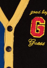 Juodas, mėlynas ir geltonas megztas kardiganas su V formos iškirpte, turintis mygtukų užsegimą, siuvinėtu "G" logotipu ir "Guess" tekstu.