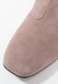Zamszowe botki za kostkę w stonowanym różu o gładkiej, lekko teksturowanej powierzchni, zaokrąglonym nosku i subtelnych ściegach w okolicy otwarcia.