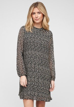 Svart blomstret kjole med lange, gjennomsiktige ermer, samlet detaljering og utsvingt kant. Har små, beige blomster på en mørk bakgrunn.