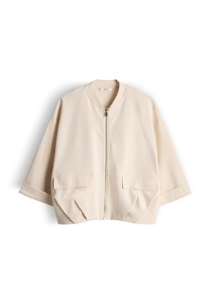 Beige kurze Jacke mit Frontreißverschluss, weiten Ärmeln, zwei aufgesetzten Klappentaschen vorne und rundem Kragen, flach auf weißem Hintergrund ausgebreitet.