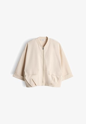 Beige kurze Jacke mit Frontreißverschluss, weiten Ärmeln, zwei aufgesetzten Klappentaschen vorne und rundem Kragen, flach auf weißem Hintergrund ausgebreitet.