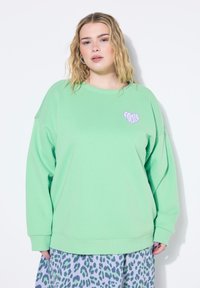 Světle zelená mikina s oversized střihem, kulatým výstřihem a dlouhými rukávy. Na přední straně se nachází fialové srdíčko s nápisem "FOCUS."