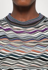 Vícebarevný pletený top s vlnitým vzorem, se černými, bílými, fialovými a modrými pruhy; žebrovaný límec s dekorativním šitím.