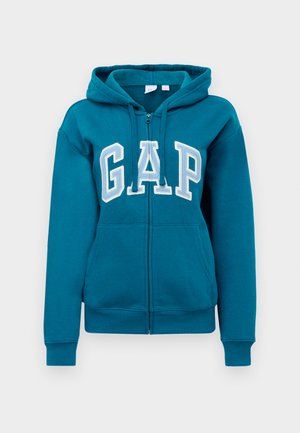 Haut à capuche zippé teal avec le logo "GAP" blanc sur le devant. Présente une capuche ajustable avec cordon de serrage et des poches avant. Tissu doux en mélange de coton.