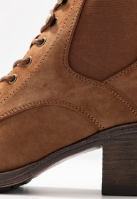 Stivale in camoscio marrone con design strutturato, punta arrotondata e tessuto a costine a contrasto. Presenta occhielli in metallo e tacco impilato in legno.