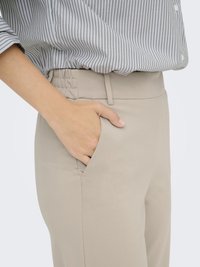 Pantalons extensibles beiges avec poches latérales, en tissu lisse et taille élastique, associés à un chemisier rayé gris et blanc.