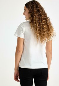 Vit bomulls-t-shirt med korta ärmar, rund halsringning och rak passform, i kombination med svarta figursydda byxor. Slät textur, minimalistisk design.