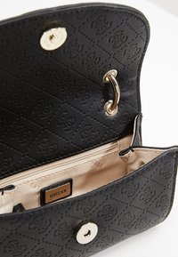 Musta nahkainen käsilaukku, jossa tikattu kuvio ja logomerkintä. Varustettu kullanvärisellä nepparikiinnityksellä ja beigen värisellä sisävuorella, jossa vetoketjutasku.