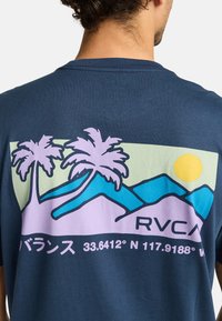 Marineblauw t-shirt met een grafisch ontwerp van palmbomen, bergen en een zon in pastelkleuren. De tekst bevat "RVCA" en coördinaten.
