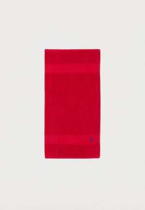 Serviette rectangulaire rouge avec deux bandes horizontales texturées et un petit logo brodé bleu marine près du bord inférieur sur un fond blanc.