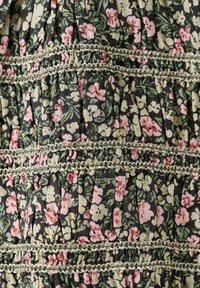 Abito floreale con uno sfondo scuro, caratterizzato da motivi rosa e verdi. Tessuto texturizzato con pieghe e dettagli di rifinitura verde.