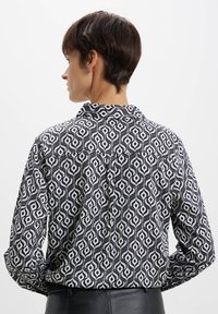 Blusa a fantasia bianco e nero con forme sinuose, maniche lunghe, colletto e tessuto leggero, vista dal retro.
