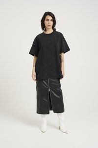 Svart oversized t-skjorte med kort erm, sammen med et knelangt svart skinnskjørt med glidelås foran, og hvite spisse ankelstøvletter.