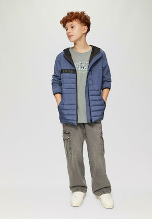 Blauwe pufferjack met een zwarte capuchon en ritssluiting, gecombineerd met een grijs graphic t-shirt en grijze cargobroek. Witte sneakers.
