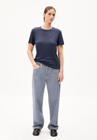 T-shirt à manches courtes bleu marine avec un col rond, associé à un jeans en denim bleu clair à coupe décontractée et des chaussures noires à semelles épaisses.