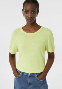 Sweter z krótkim rękawem i okrągłym dekoltem w jaskrawożółtym kolorze, charakteryzujący się miękką fakturą i luźnym krojem, zestawiony z niebieskimi dżinsowymi szortami.