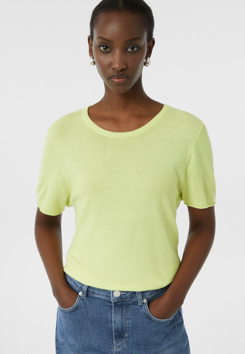 Sweter z krótkim rękawem i okrągłym dekoltem w jaskrawożółtym kolorze, charakteryzujący się miękką fakturą i luźnym krojem, zestawiony z niebieskimi dżinsowymi szortami.