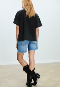 Sort oversized t-shirt med korte ærmer, lyseblå denimshorts med frynset kant og sorte knæhøje støvler med bred hæl.