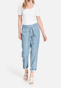 Jasnoniebieskie spodnie z chambray o luźnym kroju, z ściągniętym w pasie i podwiniętymi mankietami. Połączone z dopasowaną białą koszulą i tkanymi butami wsuwanymi.