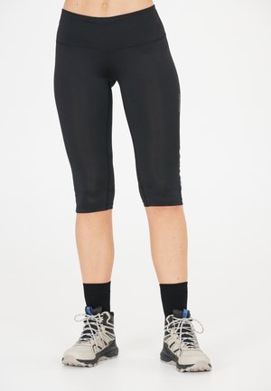  Sorte capri leggings med en glat og jævn tekstur samt en høj talje, parret med grå vandrestøvler og sorte sokker.