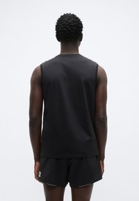 Μαύρο αμάνικο πουκάμισο απ ό βαμβάκι, με στρογγυλή λαιμόκοψη. Το φόντο είναι απλό λευκό, προσφέροντας αντίθεση στο ρούχο.