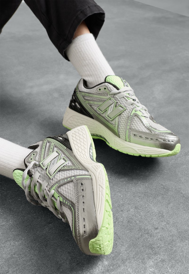 Personne portant des chaussettes blanches et des baskets grises avec des accents vert clair sur un sol gris.