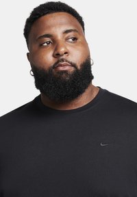 Black short-sleeve t-shirt made of smooth fabric, featuring a small black Nike logo on the chest and a crew neck design.