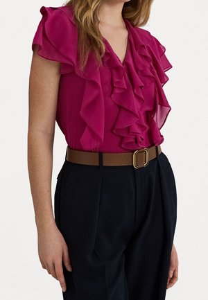 Woman wearing a sleeveless magenta ruffled blouse tucked into black high-waisted pants with a brown belt and gold buckle.