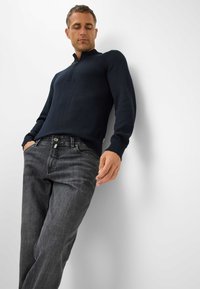 Pullover blu navy a maglia con colletto alto e polsini a coste, abbinato a jeans grigi scuri con una sottile texture e design classico a cinque tasche.
