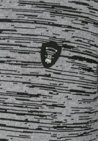 Gestrickter Pullover mit einem schwarz-grauen Streifenmuster, einer strukturierten Oberfläche und einem schwarzen, schildförmigen Logopatch auf der Vorderseite.