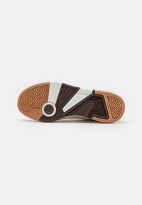 Sole of a sneaker with a segmented design. Features a brown rubber base, textured pattern, white accents, and a circular emblem.