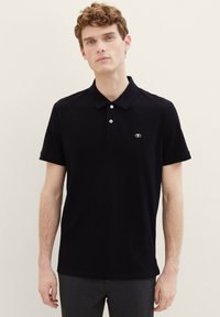 Zwarte polo gemaakt van katoen, met een klassieke kraag, een twee-knopen sluiting en een klein logo op de linkercanvas. Korte mouwen.