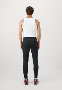 Sorte ribbede træningsbukser med en tætsiddende pasform, parret med en hvid tanktop og iført røde og sorte løbesko.