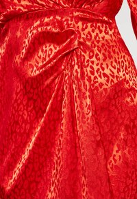 Rode satijnen jurk met een panterprint in donkerder rood. De stof heeft een gladde textuur met geplooide details en elegante draping.