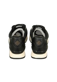 Black athletic shoes with a smooth synthetic upper, padded collar, minimalistic design, and a contrasting off-white sole. Features logo detail.