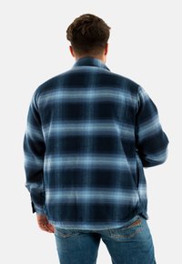 Navy blauw geruit flanellen shirt met lichtblauwe patronen, lange mouwen en een kraag, gecombineerd met denim jeans.