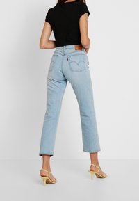 Světlé modré denimové džíny se rovný střih, zadní kapsy a hnědá kožená nášivka. Kombinované s přiléhavým černým topem a žlutými sandály na podpatku.