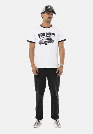 T-shirt blanc avec des accents noirs en anneau, portant le texte "VON DUTCH" et un graphique de voiture. Porté avec un jean noir et des chaussures à enfiler à carreaux.