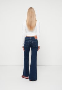 Mørkeblå denim flared jeans med et lædermærke i ryggen, der har to baglommer og rå kantkanter.