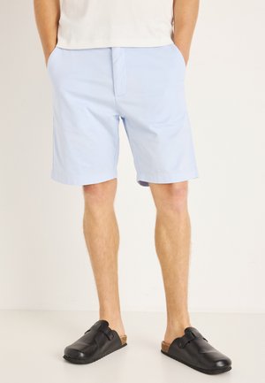 Shorts bleu clair en tissu lisse, avec deux poches latérales et une coupe droite. Associés à des sabots noirs avec un accent de sangle.