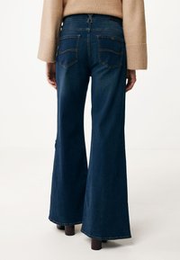 Mörkblå utsvängda denimjeans med medelhög midja, med bakfickor med synlig sömnad och en subtil textur.