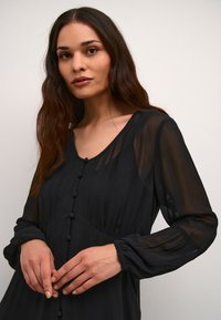 Černé, průsvitné dlouhé šaty s výstřihem do V, knoflíkovými detaily na přední straně a nařasenými manžetami, které mají splývavý siluetu.