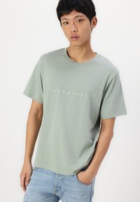 Mintgrønn bomulls T-skjorte med korte ermer, med hvit tekst "JACK & JONES" over brystet, avslappet passform og rund hals. 