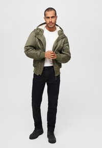 Olivgrön bomberjacka med en faux shearling-foder, dragkedja fram, ribbade ärmslut och sidofickor, kombinerad med svarta jeans och svarta stövlar.