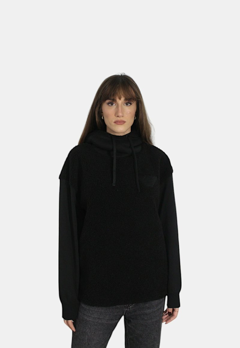 Felpa nera con un frontale in pile texturizzato e maniche lunghe, caratterizzata da un collo alto e una minimalistica etichetta sul petto.